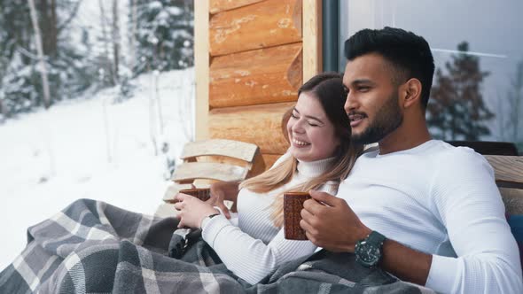 Happy Young Couple Hugging Covered with Blanket on the Outdoors Bench alt
