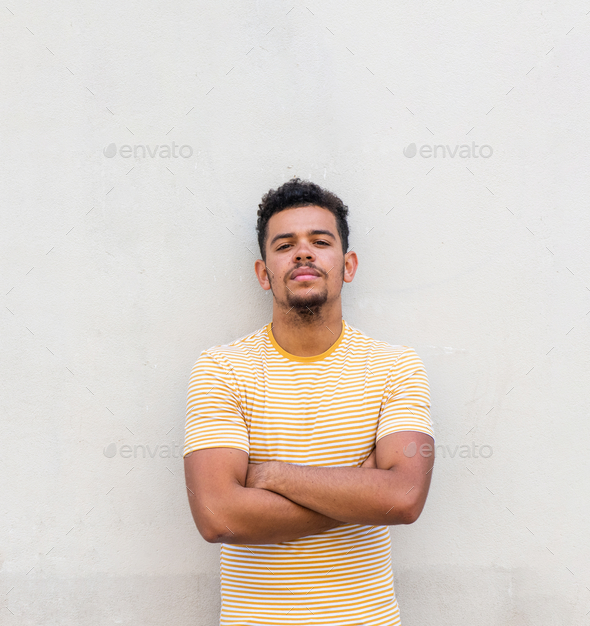 cool young mixed race man staring with arms crossed by white background