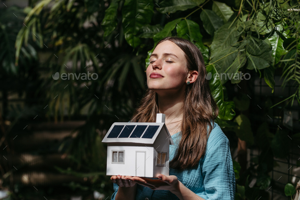 Young woman in jungle holding paper model of house with solar