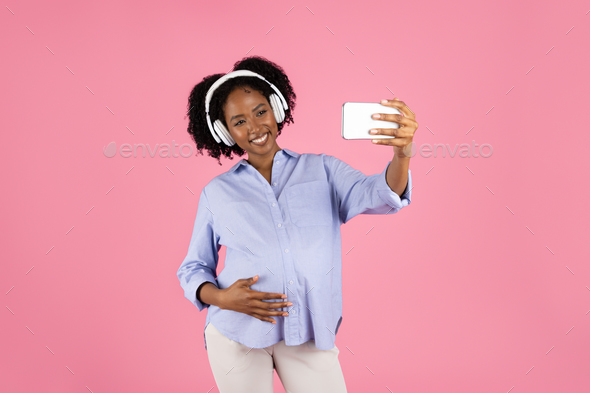 Happy millennial african american curly pregnant woman with belly in  headphones takes selfie on Stock Photo by Prostock-studio