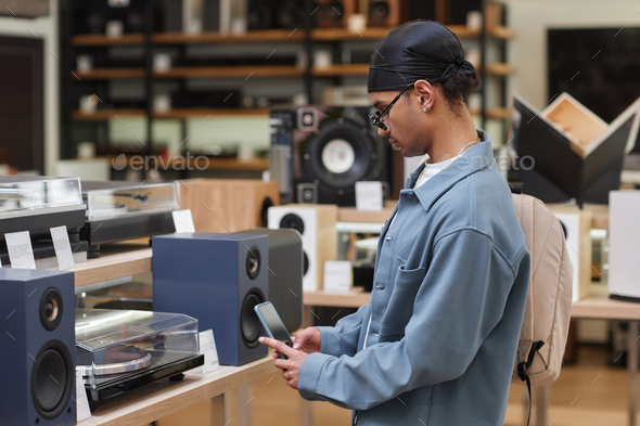 Black man looking at vinyl record player in music store and taking picture
