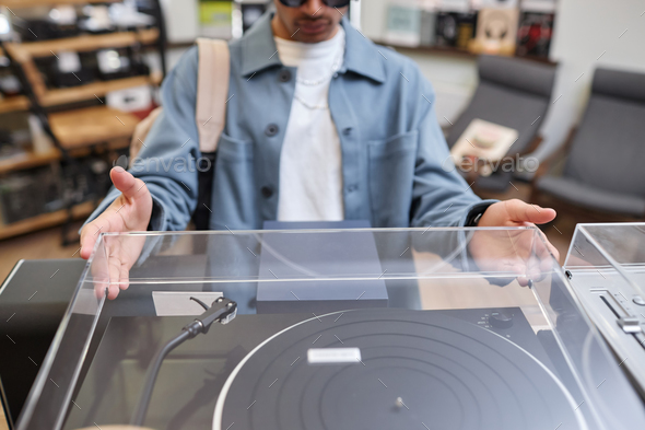Closeup of black young man opening lid pn record player in music store