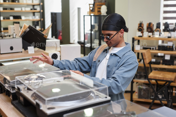 Side view black young man choosing record player in music store