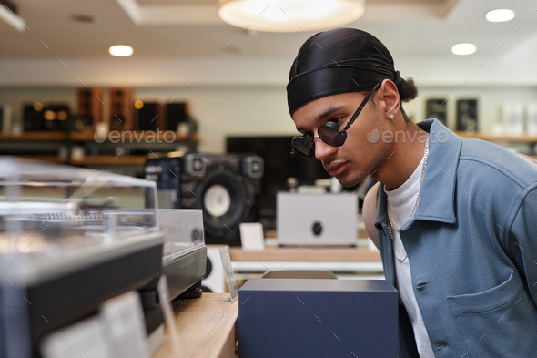 Side view black young man looking at record players and equipment in music store