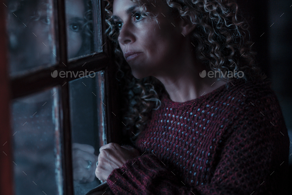 Serious and sad woman looking outside the window at home indoor. Concept of insomnia and night fear.