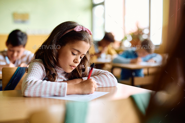 Hispanic schoolgirl writing an exam during a class in the classroom.