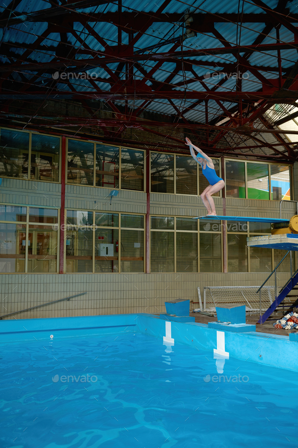 Sportswoman standing on diving board at public swimming pool ready to jump