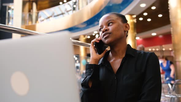 Attractive African American Woman Talking on Mobile Phone While Using Laptop alt
