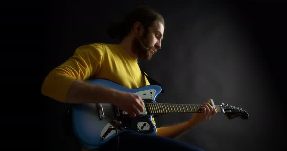 Male Guitarist in a Yellow Jumper Plays an Electric Guitar on Black Background alt