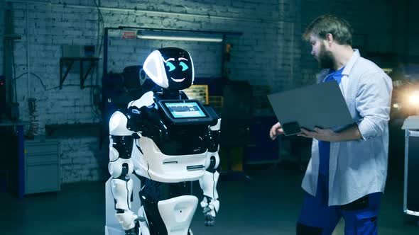 Robotic Research Engineer with a Laptop Is Observing a Robotlike Machine alt