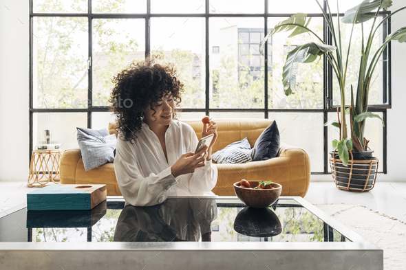 African american woman browsing social media while eating strawberry in a bright loft apartment