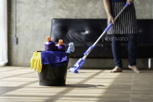 A young butler cleans the floor, mops the floor, carries a mop and a plastic bucket with brushes, gl