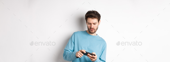 Young man playing video games on smartphone, tilt body and tap mobile screen, standing joyful over