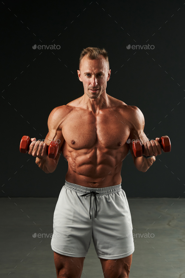 caucasian man trains hard with dumbbells. beautiful body, perfectly pumped muscles, perfect abs