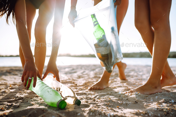 Three young girls pick up trash on the beach. Environmental pollution. Ecological problem.
