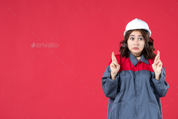 Half body shot of surprised female builder in uniform with hard hat and crossing her fingers on