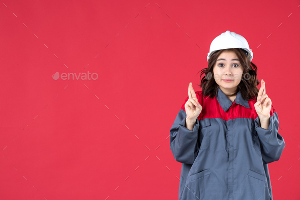 Half body shot of uncertain female builder in uniform with hard hat and crossing her fingers on