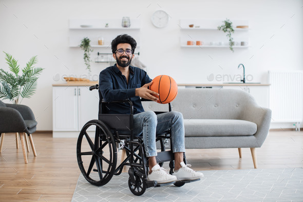Adult in wheelchair holding basketball in room interior