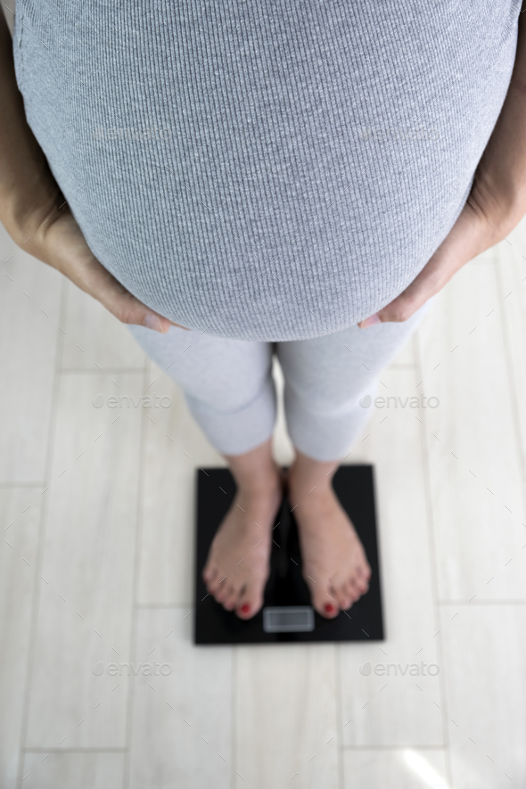 Pregnant woman on scales at home check her weight gain. Weight control during pregnancy. Stock