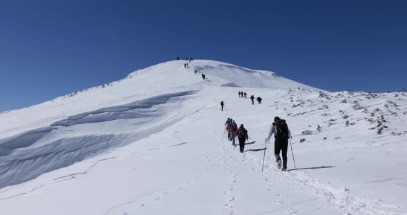Hikers walking in line towards the peak during a winter sunny day. Snow covered mountain.