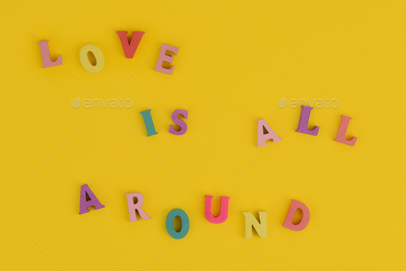 Love is all around composed of wooden letters on a yellow background.