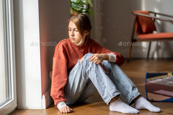 Upset teenage girl sit on floor suffer worried about bullying at school, bad relations with parents