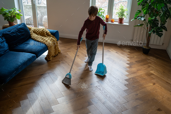Child boy sweeps floor do house chores, domestic cleanup. Habit of cleaning house since childhood