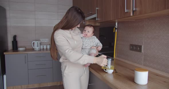 Mom Makes Tea In The Kitchen And Holds The Baby In Her Arms
