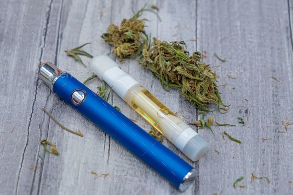 CDB. Cannabis oil extract In Vape pen cartridge and marijuana buds.  Medicinal weed Stock Photo by wirestock
