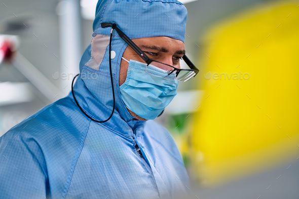 Male in a blue medical scrub suit and glasses looking downwards