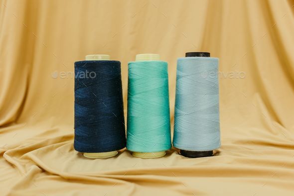 Close-up shot of three spools of different colored thread on a beige cloth