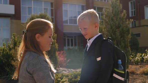 Happy Young Woman Holds the Hands of a Schoolboy Little Son Near the School alt