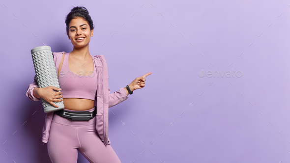 Horizontal shot of pleased Iranian woman dressed in sportswear poses with massage roller for back