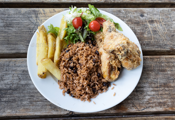 Chicken in batter with rice, beans, flour, French fries and mixed salad on a wooden table.Venezuelan