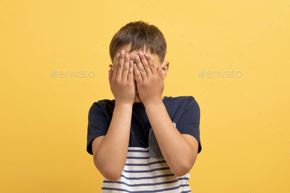 Shy little boy feeling ashamed, cover face with palms