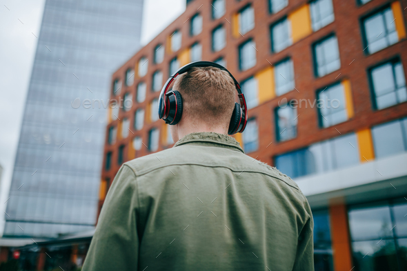 Rear view of man enjoying music while walking in the city