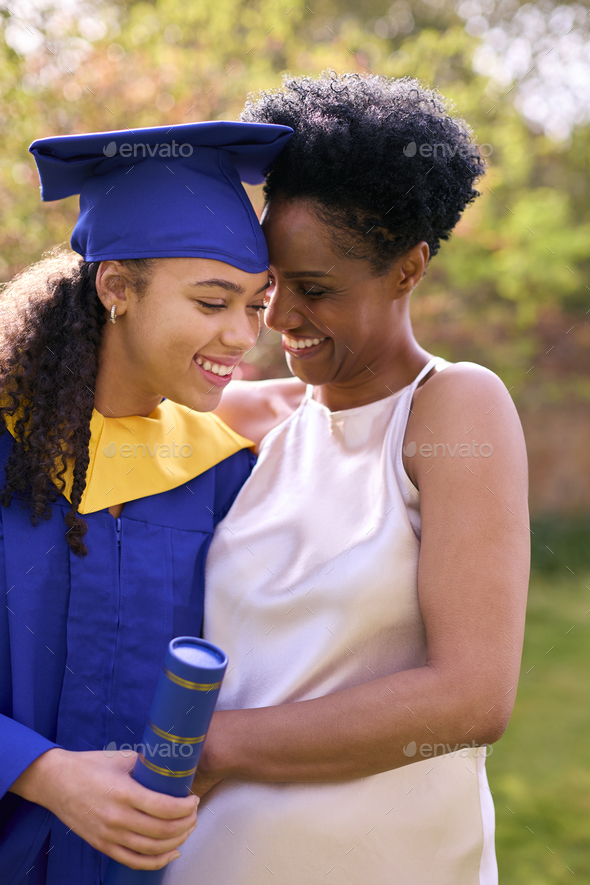 Proud Mother Celebrating With Teenage Daughter Wearing Graduation Robes Outdoors