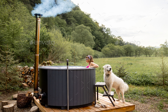 Woman bathing in hot tube, while resting with her dog on nature
