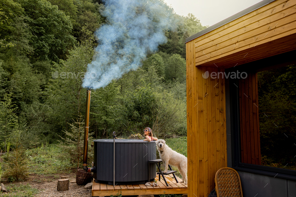 Woman bathing in hot tube, while resting with her dog on nature