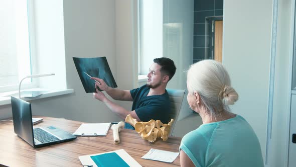 Surgeon explaining diagnosis with skeleton model and X-ray pictures