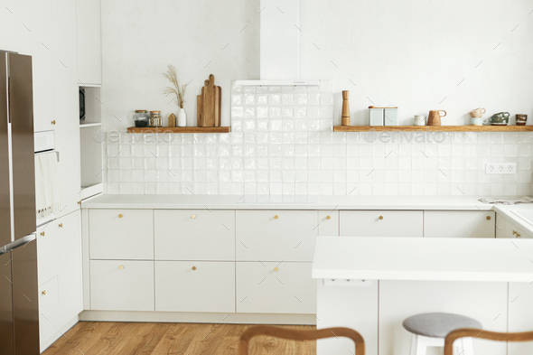 Modern kitchen interior. Stylish white kitchen cabinets with brass knobs, granite island, appliances