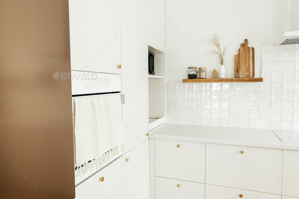 Stylish white kitchen cabinets with brass knobs, wooden shelves with utensils and appliances