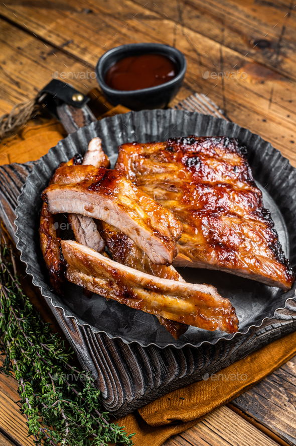 Smoked pork spare ribs glazed in BBQ sauce in a steel plate. Wooden background. Top view
