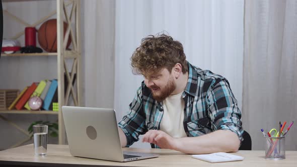 Young Man in Checkered Shirt Typing on Laptop Keyboard and Enjoying Good News or Deal alt