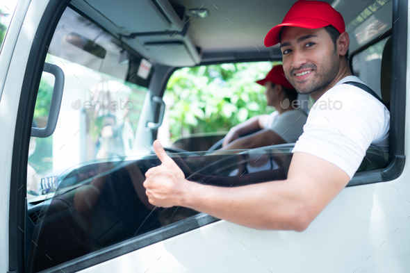 Smiling delivery man showing thumbs up while sitting behind the car door