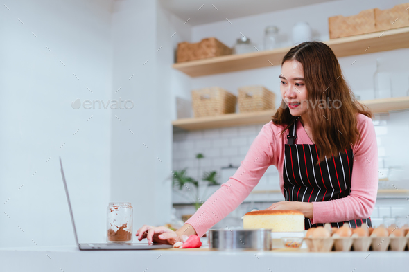 Woman Making and Decorating a Cake with the Aid of her Laptop in the Kitchen