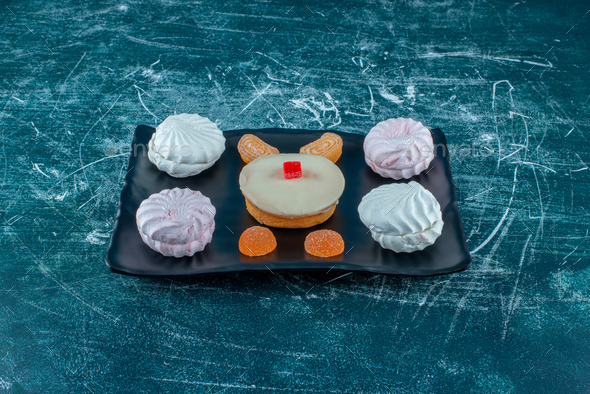 Cookies and marmelades around a white chocolate topped cake on a platter on blue background