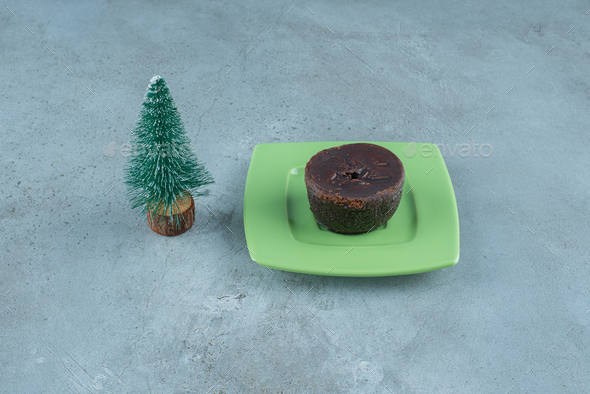 Small chocolate cake on a platter next to a tree figurine on marble background