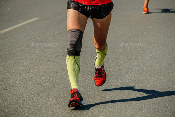 close-up legs male runner in compression socks and knee pads running marathon race