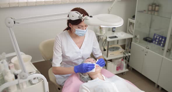 Close Up of Female Professional Cosmetologist in Blue Gloves Cleaning Face of alt
